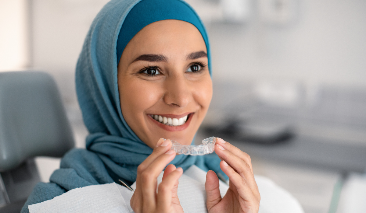 young woman holding an invisalign tray at her dentist's appointment