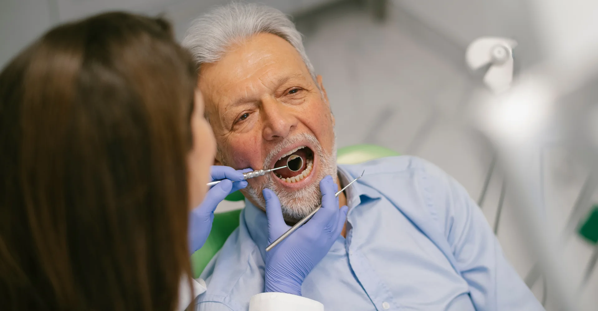 Dentist examines a patient’s mouth with a dental mirror.